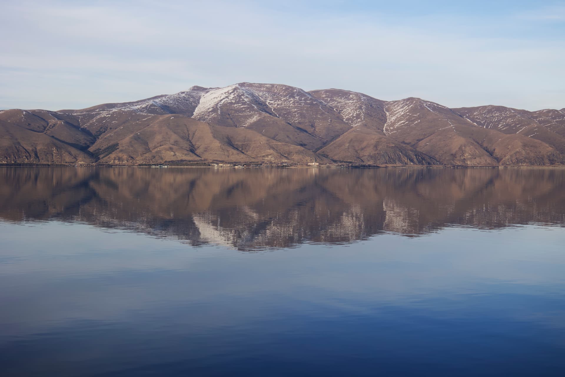 Lake Sevan reflecting snow-dusted mountains under a pale blue sky, Armenia