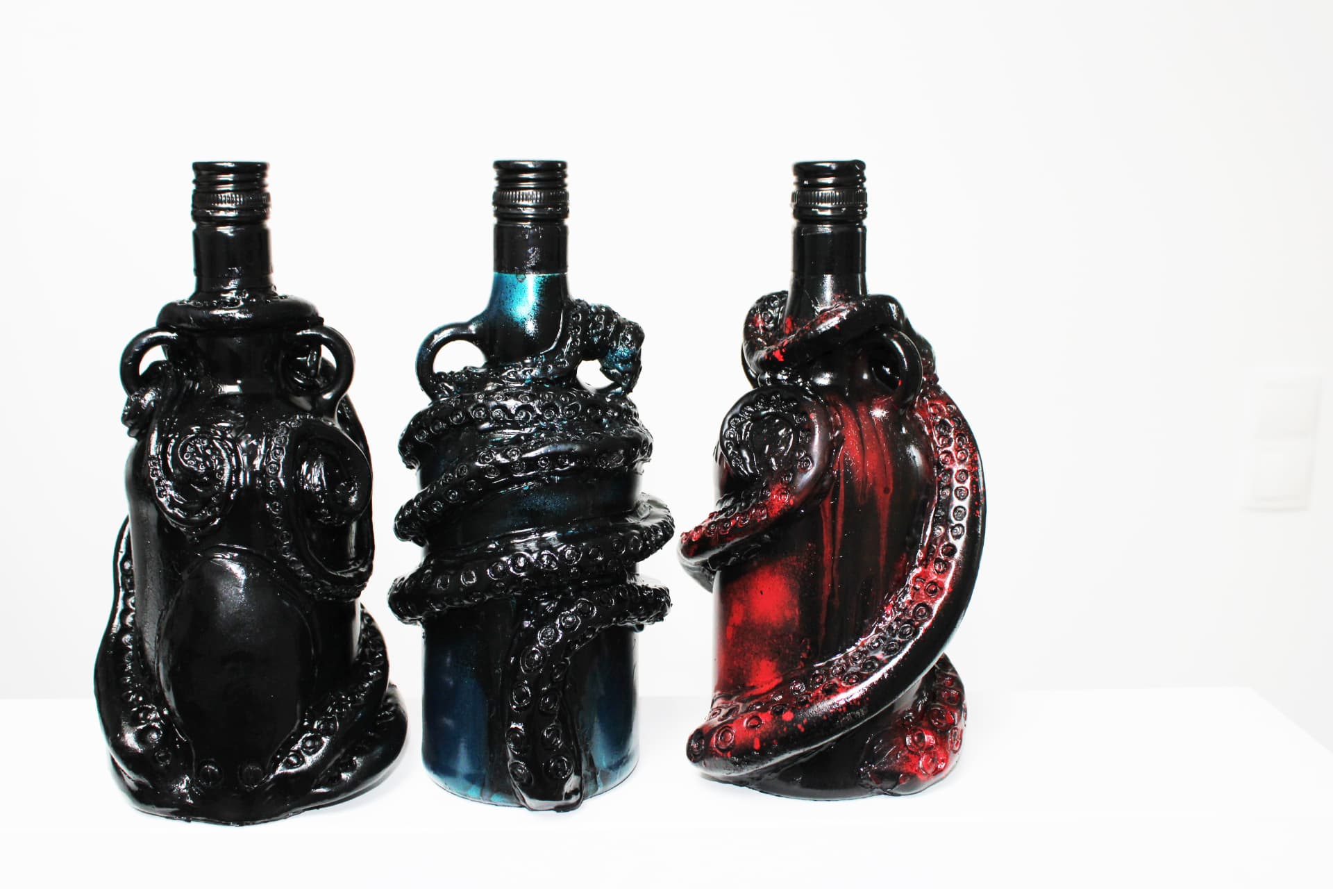 Three Kraken rum bottles sculpted with dark tentacles, displayed side by side against a white background.