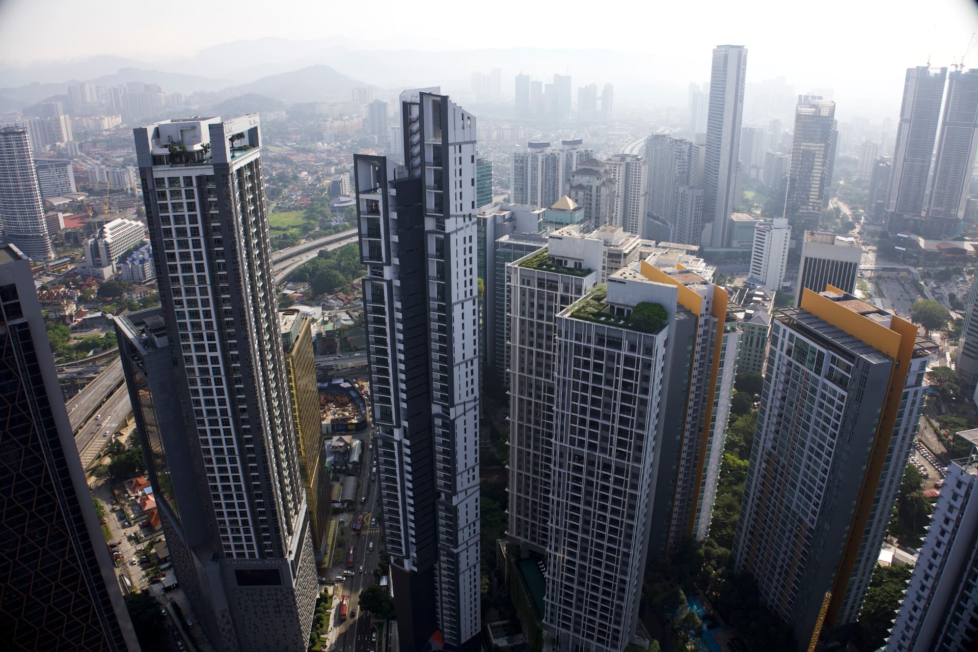 Modern high-rise towers of the Kuala Lumpur skyline rising above highways and distant hazy mountains, Malaysia