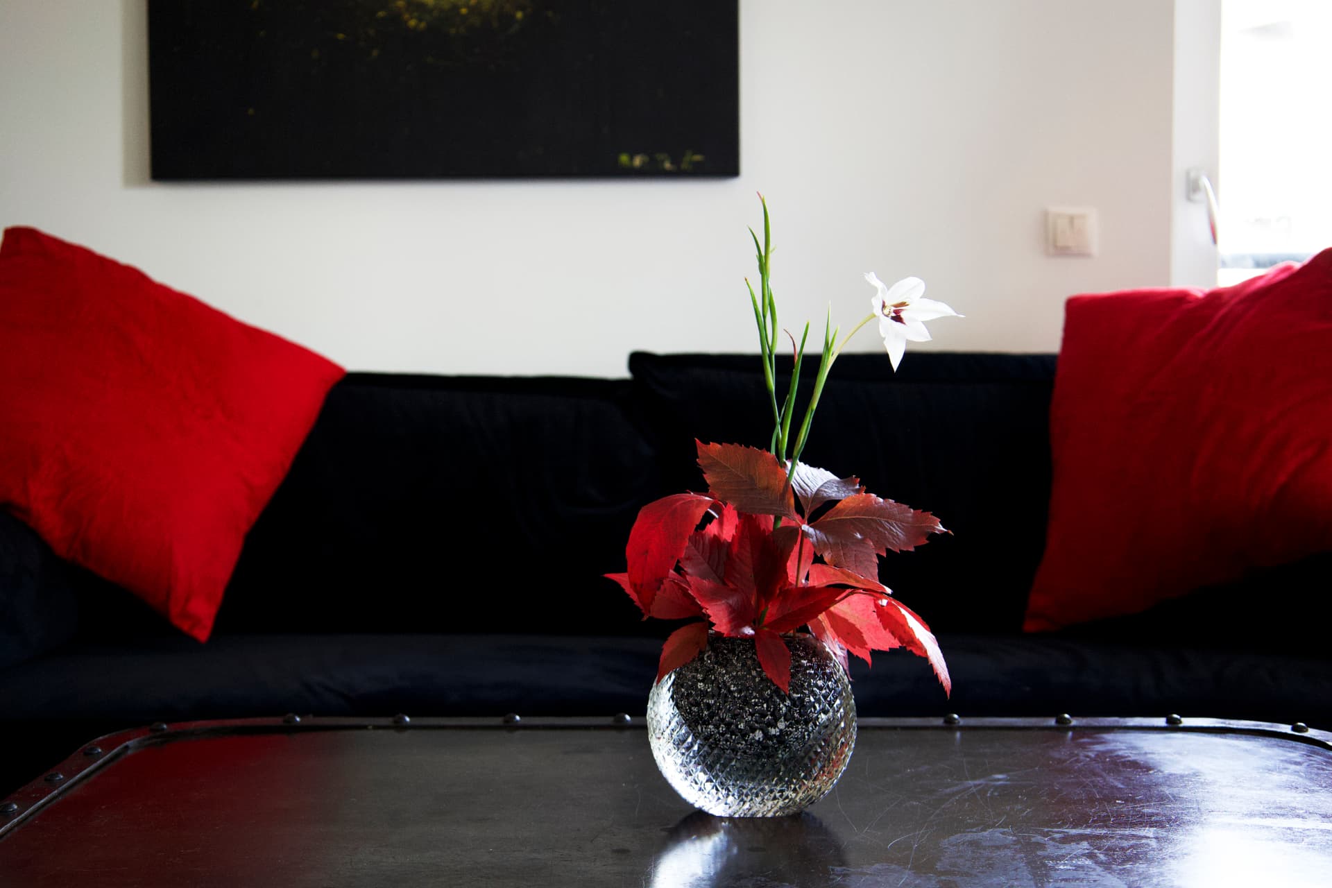 An ikebana arrangement with red leaves and a white lily in a cut-glass vase, on a dark table.