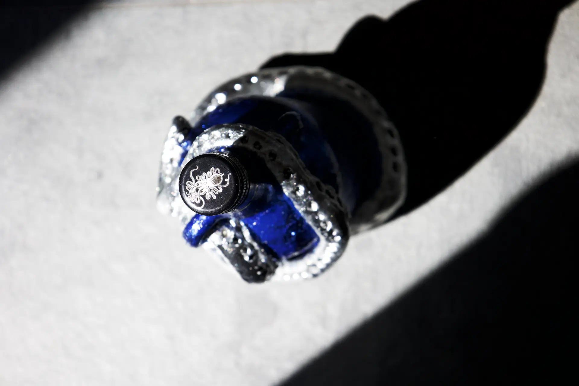 A glossy blue Kraken rum bottle decorated with silver sculpted tentacles and sparkling details, viewed from above on a light surface.