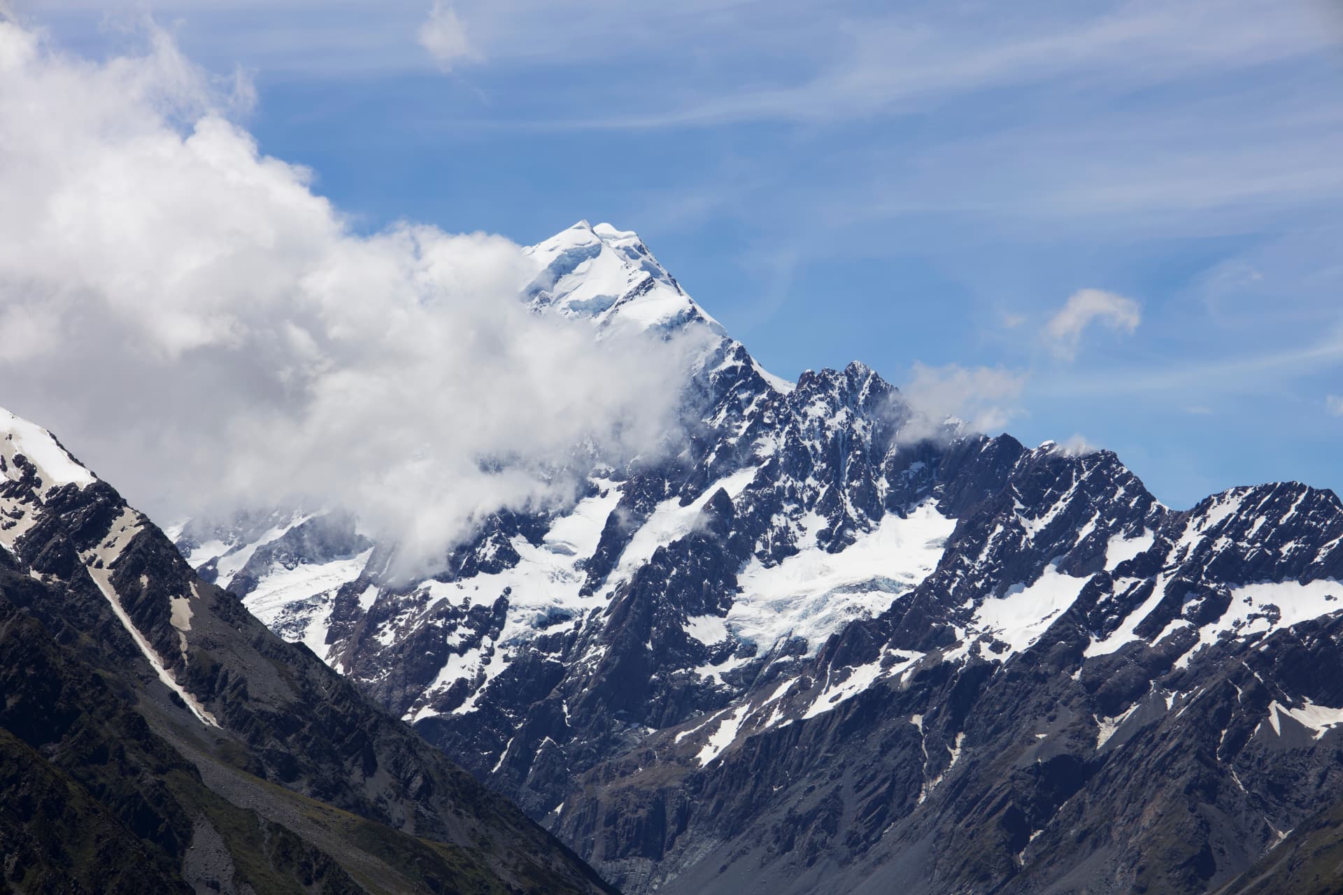 A close-up view of Mount Cook summit partially wrapped in clouds with glaciers and ridges, New Zealand
