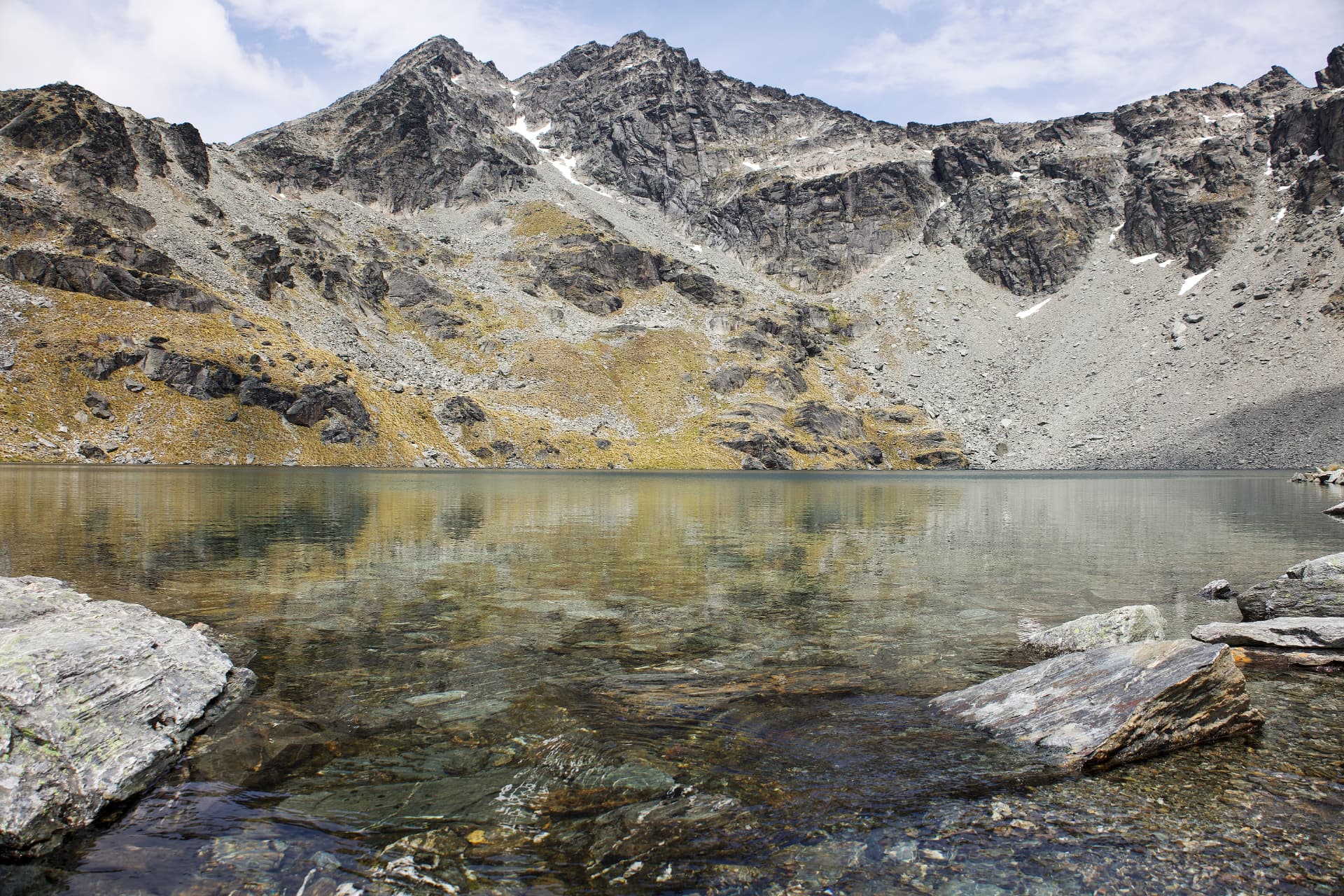 The clear, reflective water of Lake Alta surrounded by rocky alpine peaks, New Zealand