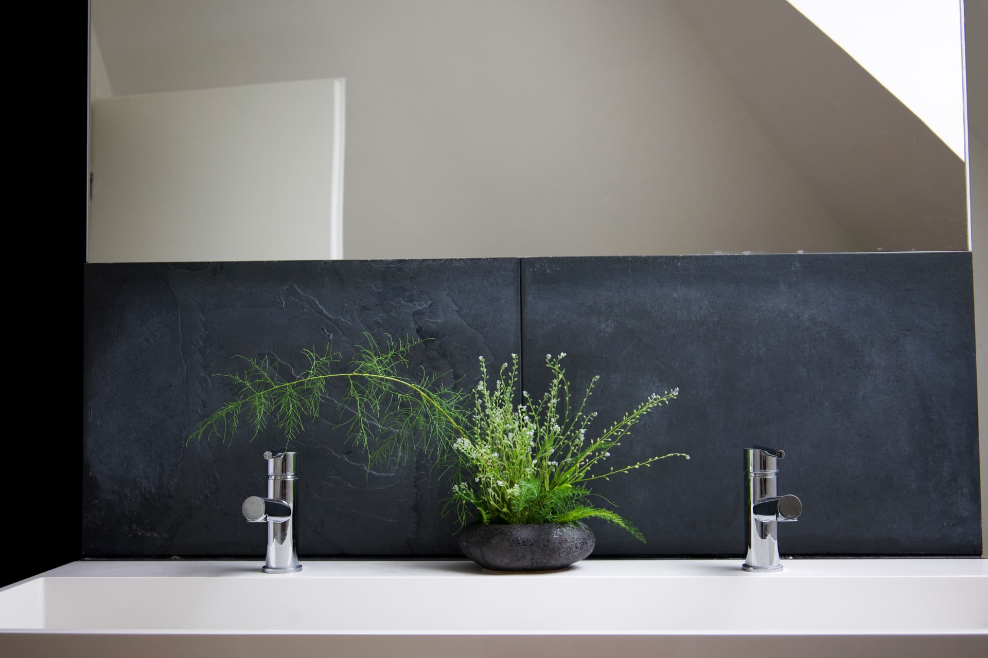 A minimalist ikebana with green fennel and tiny white flowers in a dark bowl against slate.