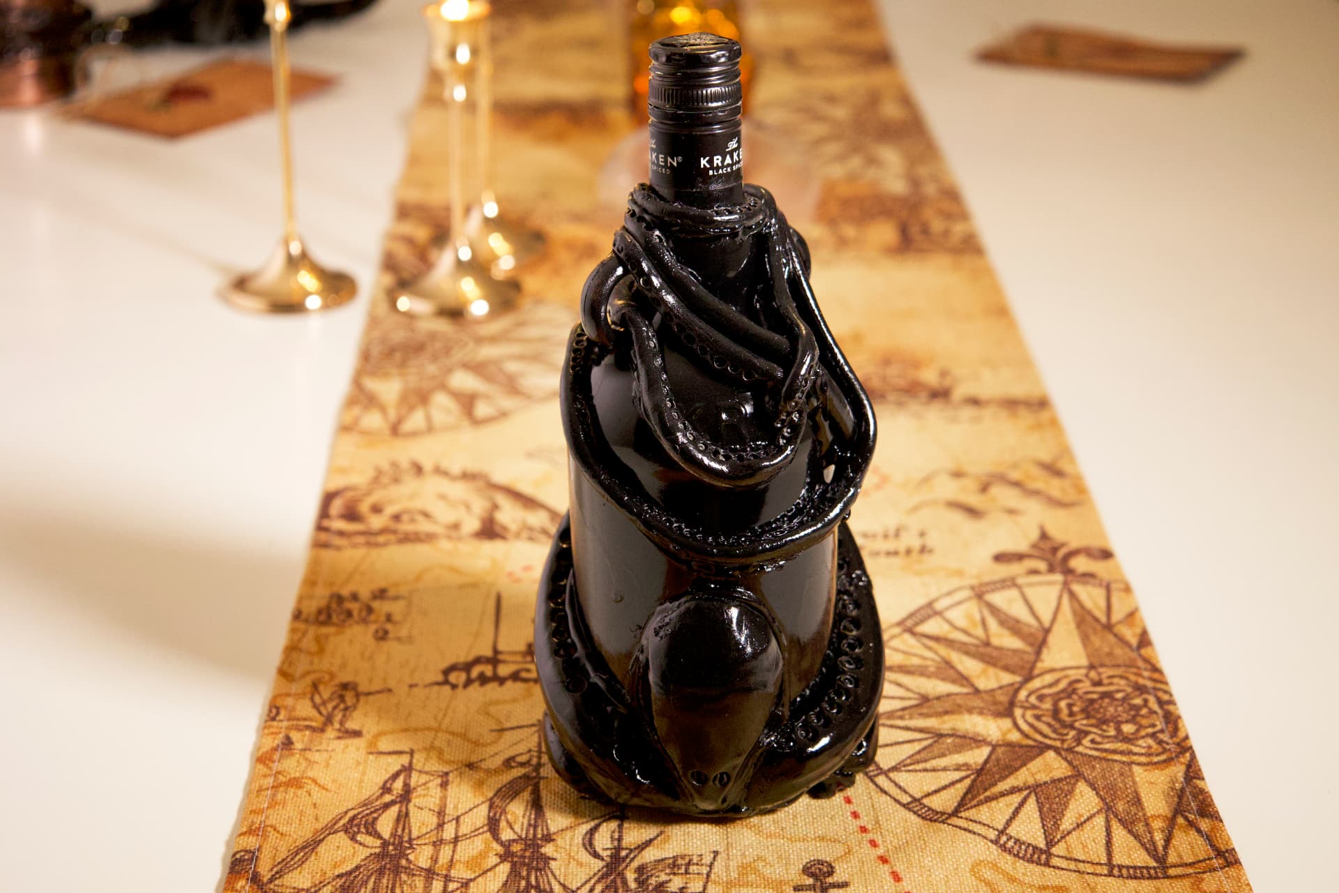 A black Kraken rum bottle sculpted with dark tentacles, displayed on a vintage map table runner with candlelight.
